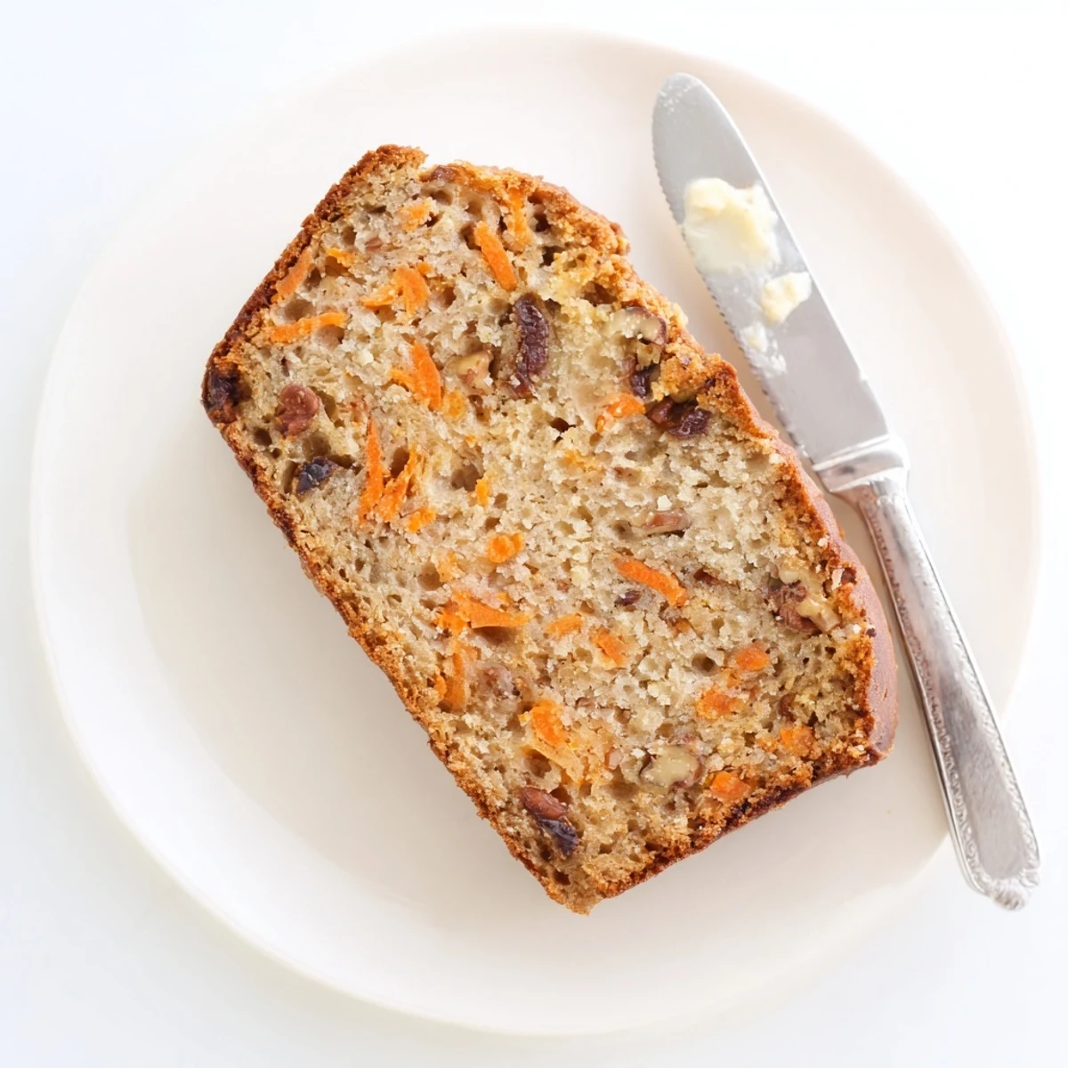 Golden brown carrot cake banana bread loaf sliced on a wooden cutting board with visible grated carrot specks