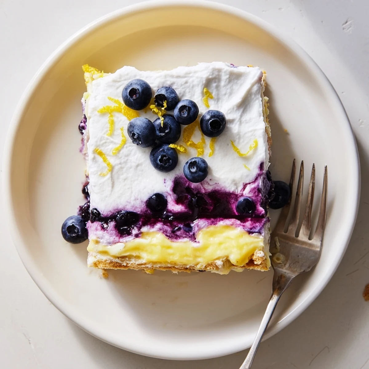 Lemon blueberry lasagna recipe garnished with whipped cream and bright lemon zest