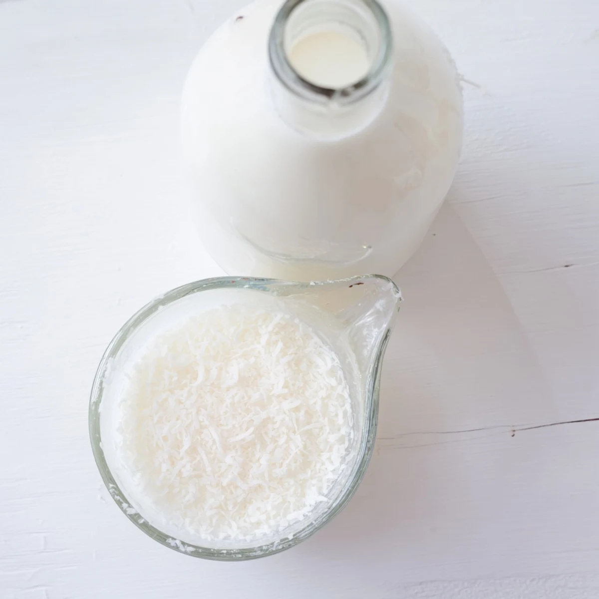 Glass bottle of creamy homemade coconut milk poured into a clear measuring cup