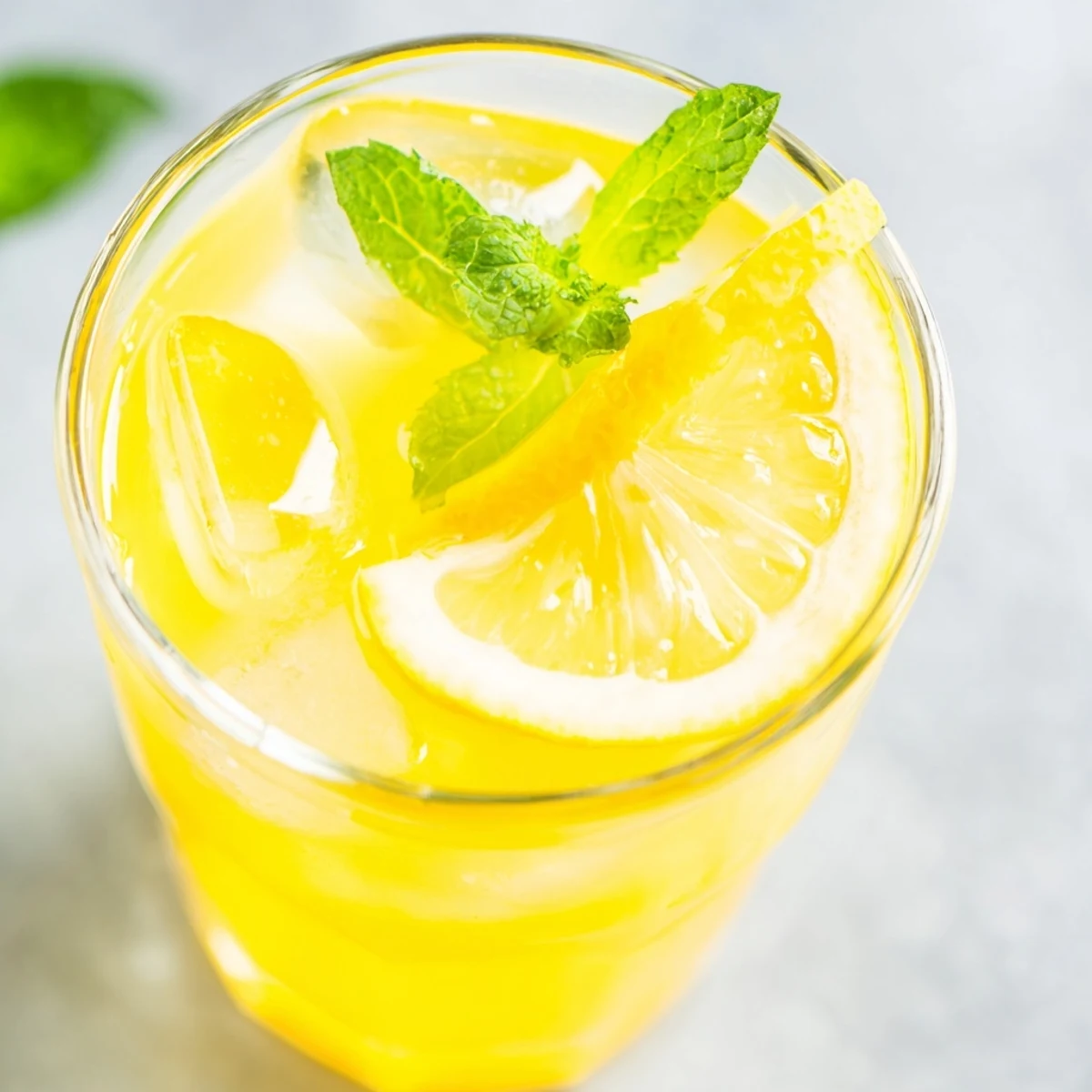 Glass of chilled lemonade garnished with fresh mint leaves and a lemon wheel on the rim.