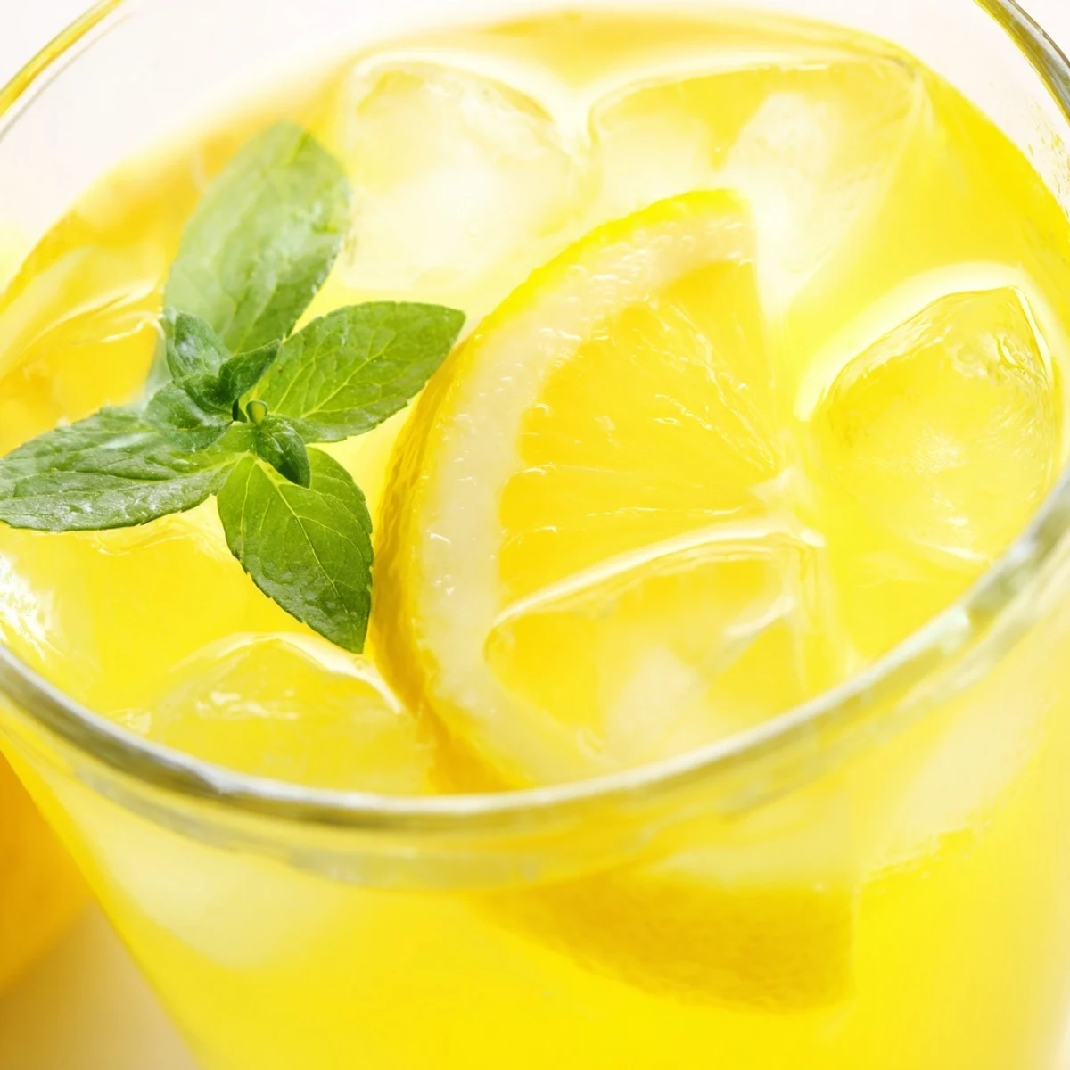 Refreshing lemonade drink with floating ice cubes and citrus slices in a transparent glass pitcher.