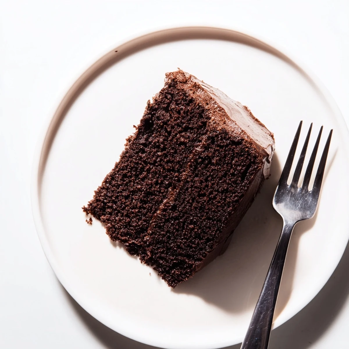 Slice of chocolate cake with mayonnaise revealing soft texture on white serving plate