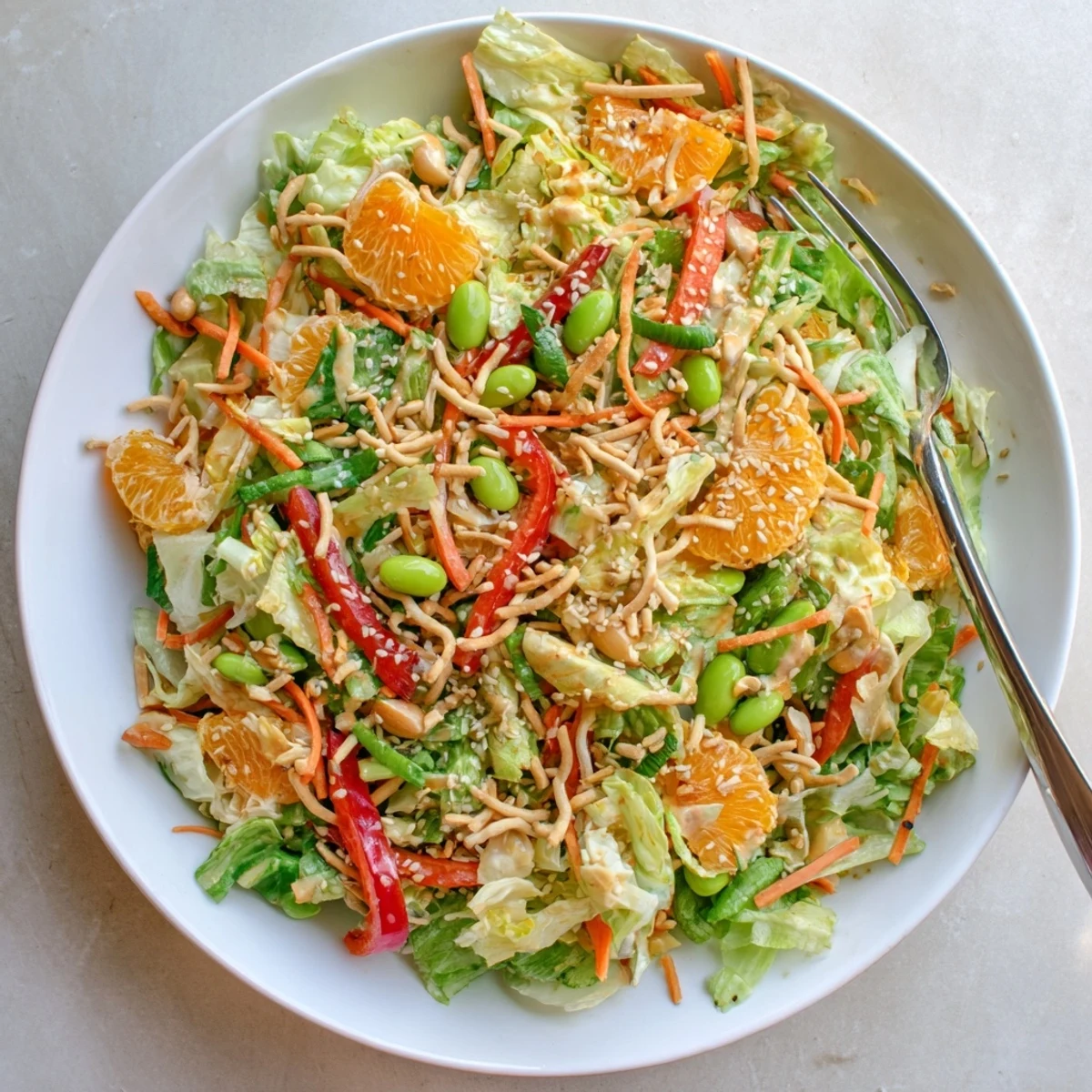 Close-up of Mandarin Sesame Crunch Salad drizzled with savory-sweet dressing on a white serving plate