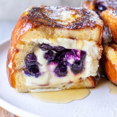 Thick slice of blueberry cheesecake stuffed French toast dusted with powdered sugar